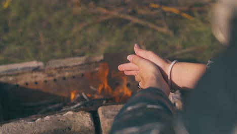girl-tourist-heats-hands-at-burning-bonfire-backside-closeup