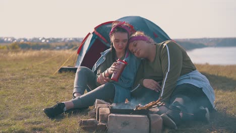 lesbian-couple-rests-at-burning-bonfire-near-blue-tent