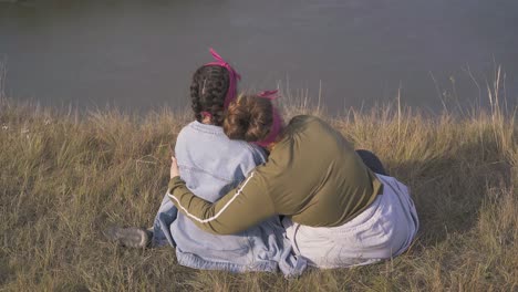 women-hug-having-date-on-steep-bank-of-river-in-evening