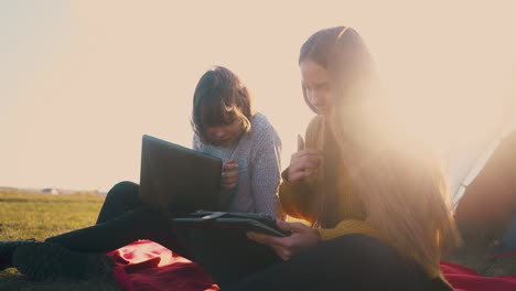 smiling-women-with-tablet-and-laptop-at-tent-against-sunset
