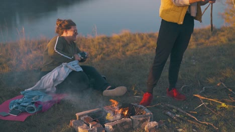 man-puts-woods-in-bonfire-near-overweight-girl-at-sunset