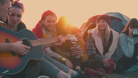 happy-hikers-listen-to-guitar-sitting-at-bonfire-in-camp
