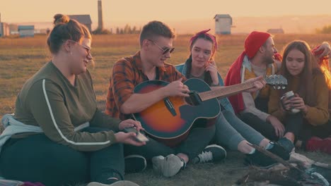 guy-plays-guitar-resting-with-friends-in-camp-at-sunset