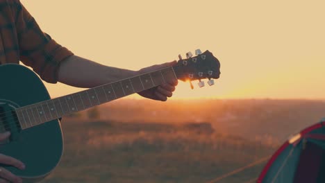 close-man-hands-with-guitar-in-tourist-camp-at-sunset
