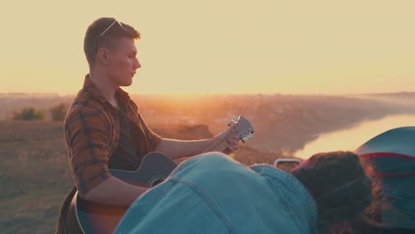 man-in-glasses-plays-guitar-to-happy-friends-near-bonfire