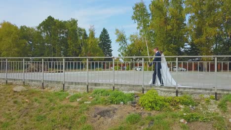 newly-wedded-couple-walks-along-fence-in-green-park