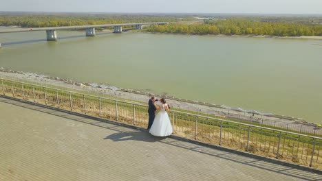 just-married-couple-at-handrail-on-hill-at-river-aerial-view