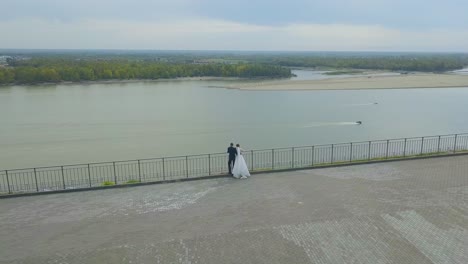 newlywed-couple-looks-at-calm-river-from-hill-bird-eye-view