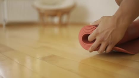 Male-hands-unfolding-red-yoga-mat-on-wooden-floor