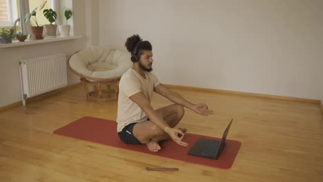 Mixed-race-man-in-headphones-meditates-in-front-laptop-with-instructor