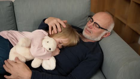 Little-girl-with-toy-sleeping-on-his-grandfather's-chest-in-the-living-room