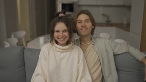 Smiling-millennial-couple-home-owners-sitting-on-cozy-sofa,-showing-keys-to-camera,-feeling-excited