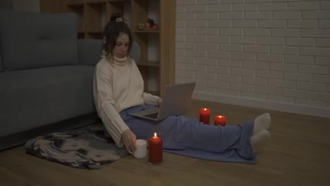Junge-Frau-Arbeitet-An-Einem-Modernen-Laptop,-Während-Sie-In-Einem-Gemütlichen-Raum-Bei-Kerzen-Sitzt
