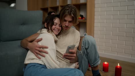 Romantic-couple-sitting-on-the-floor-together,-looking-on-smartphone-screen