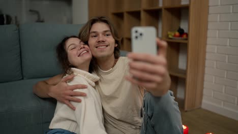 Hübsches-Paar,-Das-Zusammen-Auf-Dem-Boden-Sitzt-Und-Ein-Selfie-Mit-Dem-Smartphone-Macht