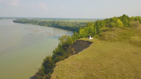 just-married-couple-enjoys-river-view-from-steep-bank-aerial