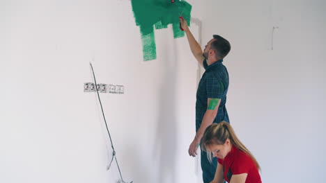 man-paints-room-white-wall-with-green-young-woman-watches