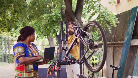 Couple-using-laptop-to-repair-bike-wheel