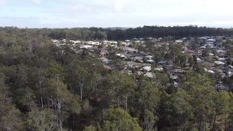 Drone-flying-over-bushland-towards-residential-estate-revealing-private-homes-in-the-background