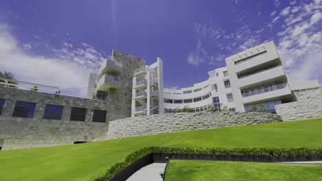 Panning-right-view-of-the-The-Getty-Center-with-blue-skies,-some-white-clouds,-and-bright-green-grass