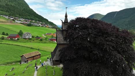 Hopperstad-Stave-Church-at-Vik-Sogn-Norway---Aerial-orbit-revealing-building-from-behind-tree---Tourists-on-guided-tour-walking-outside---60-FPS