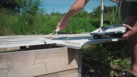 Cropped-Image-of-A-Man-Painting-Planks-Of-Wood-With-White-Paint-Using-Roller-Brush-Outdoor