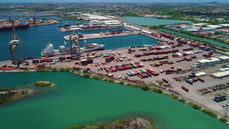 Panoramic-aerial-orbit-of-shipping-container-docked-in-port-offloading-cargo-with-cranes,-Curacao