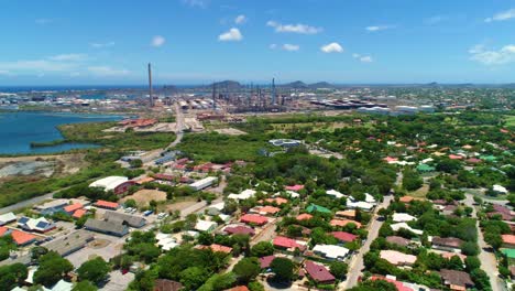 Aerial-dolly-to-oil-refinery-near-ocean-port-harbor-behind-neighborhood-suburb,-Curacao