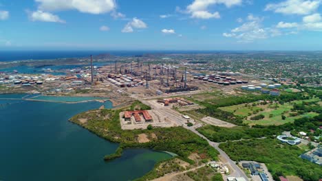 Panoramic-aerial-overview-of-oil-refinery-industrial-zone-next-to-luxury-golf-course,-caribbean
