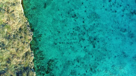 Bird's-eye-view-perspective-of-cliffside-and-water-ocean-ripples-in-clear-caribbean-sea