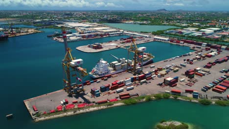 Shipping-container-port,-two-cranes-and-a-small-boat-docked,-sunny-day-on-Curacao