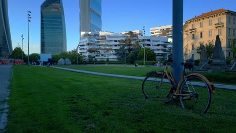 Bicycle-tied-to-the-pole-in-Piazzale-Giulio-Cesare,-in-the-background-the-skyline-of-Zaha-Hadid's-housing-complex,-CityLifeMilano,-Milan,-Italia