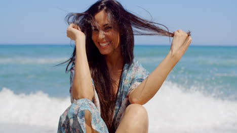 Happy-Woman-Sitting-at-the-Beach-Holding-her-Hair