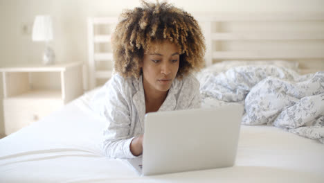 Woman-Looking-At-Laptop-In-Bed-At-Home