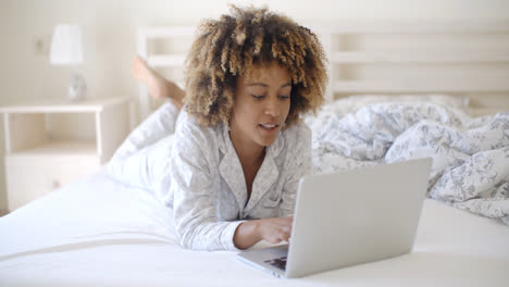 Woman-Looking-At-Laptop-In-Bed-At-Home
