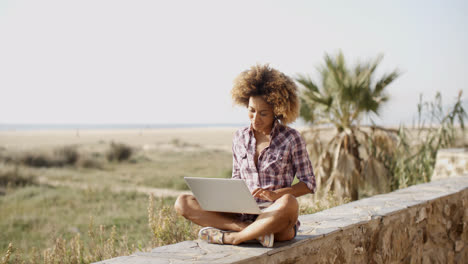 Woman-With-Laptop-Sitting-On-Stone-Wall