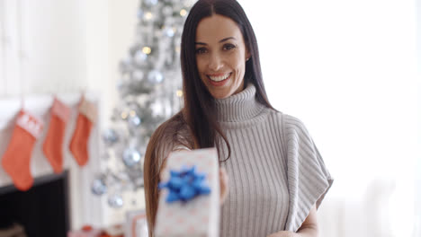 Smiling-young-woman-holding-out-a-Christmas-gift