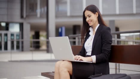 Woman-sitting-with-laptop-on-bench-outdoors