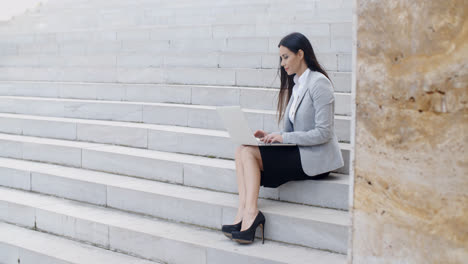 Smiling-woman-using-laptop-on-stairs