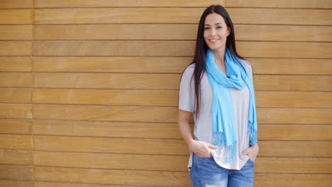 Smiling-woman-with-hands-in-pockets-near-wood-wall