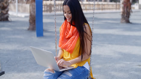 Stylish-woman-sitting-on-a-swing-with-her-laptop