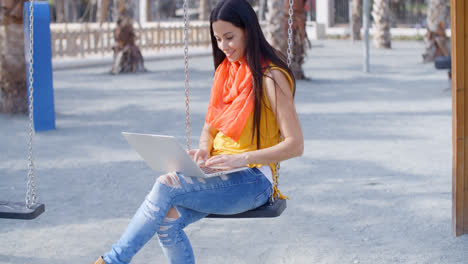 Stylish-woman-sitting-on-a-swing-with-her-laptop