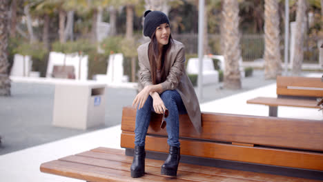 Fashionable-young-woman-sitting-waiting-on-a-bench