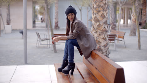 Fashionable-young-woman-sitting-waiting-on-a-bench
