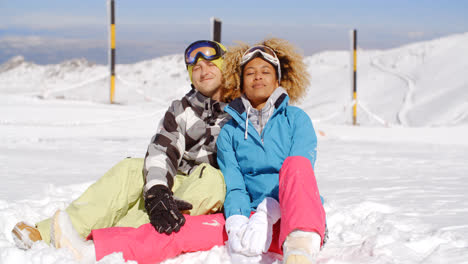 Couple-sitting-in-snow-on-ski-slope