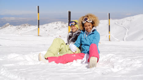 Couple-sitting-in-snow-on-ski-slope
