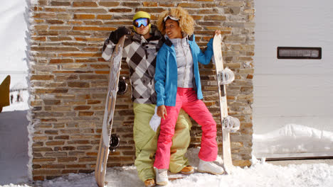Close-couple-posing-with-snowboards-against-garage