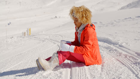 Frau-Im-Orangefarbenen-Schneeanzug-Sitzt-Auf-Der-Skipiste