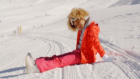 Woman-in-orange-snowsuit-sitting-on-ski-slope