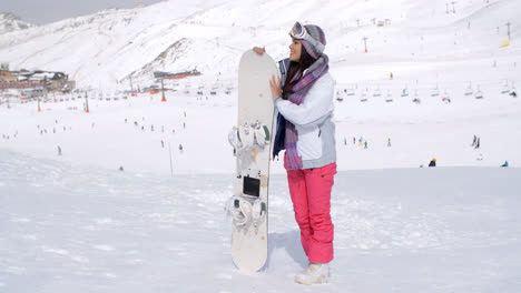 Young-woman-standing-waiting-with-her-snowboard